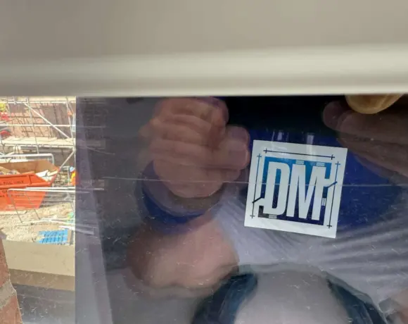 Drywall Machines logo card held against a glass panel on a construction site