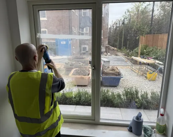 Technician in a hi-vis vest polishing a patio door glass panel on site