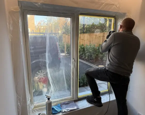 Glass polisher working on a scratched patio door pane inside a masked room